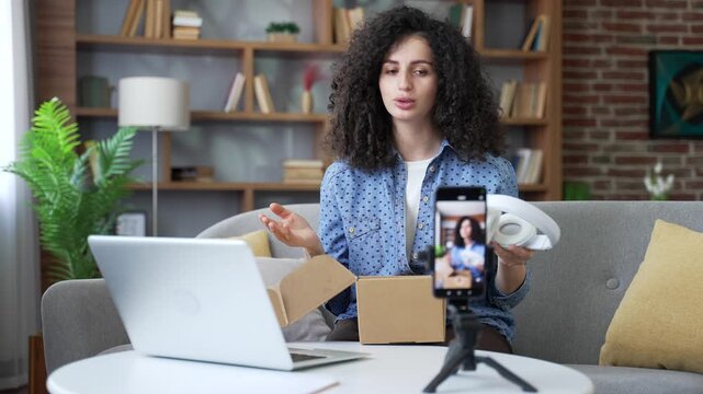 Female vlogger or blogger recording video blog while unboxing new wireless headphones in home office Influencer conducts live streaming by phone leaving review about product giving feedback and advice