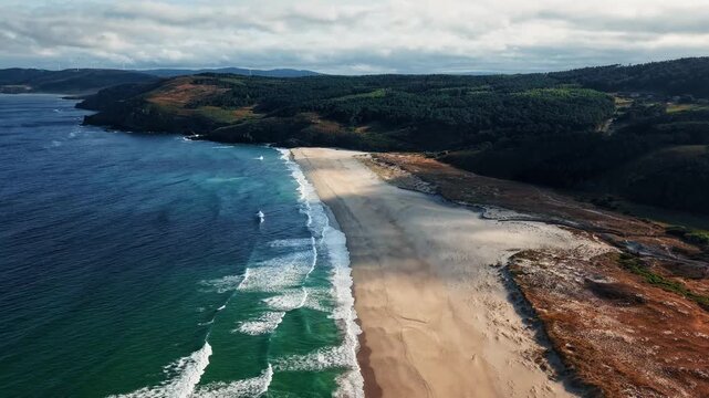 Drone flying above Praia do Rostro on the wild Galicia coast with Atlantic waves rolling along the remote sandy shoreline.