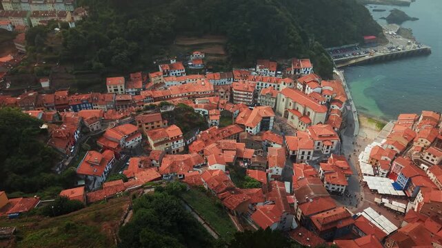 Drone orbit revealing the red roof houses of Cudillero fishing village and harbor along the Asturias coast in northern Spain.