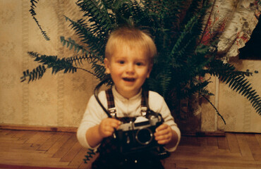 Little boy holding vintage film camera, authentic 1990s family snapshot, retro childhood photography © XArt