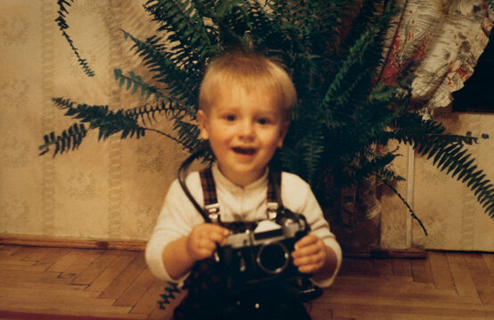 Little boy holding vintage film camera, authentic 1990s family snapshot, retro childhood photography