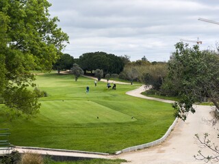 Fototapeta premium Aerial view of green golf course with winding path and trees under blue sky.