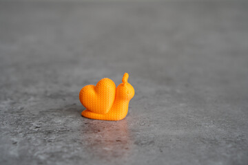 3D printed orange snail on the grey surface © Margarita