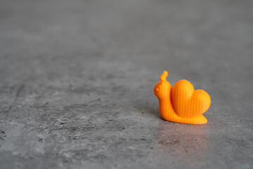 3D printed orange snail on the grey surface © Margarita