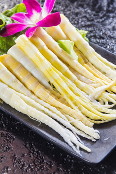 A black rectangular plate with neatly arranged bamboo shoots garnished with lettuce and a purple flower.