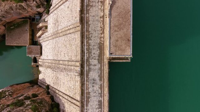 Top-down aerial view of Benag&eacute;ber Dam on the Turia River in Valencia, Spain, showing the concrete gravity structure, spillway crest and turquoise reservoir waters