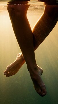 Vertical video: Floating adult legs and feet uncrossing after leg shift at lake surface, sunlight
