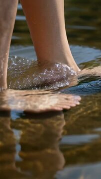 Vertical video: Stepping bare feet at river edge, making ripples, splashes, reflections, copy space
