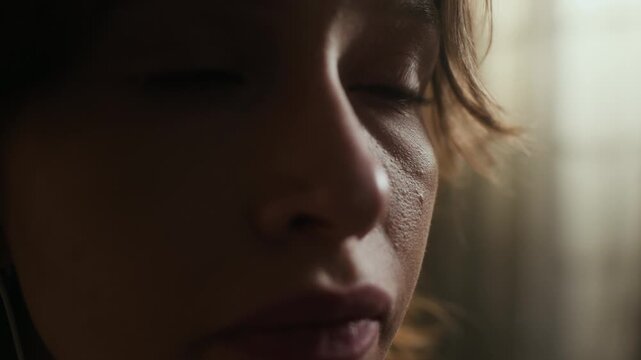 Big close up of gen Z Caucasian girl sobbing while listening to music in earphones and feeling lonely at night indoors
