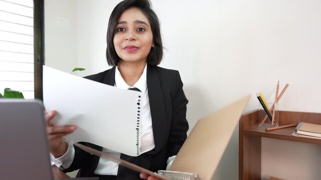 Close up portrait of happy successful young Indian working business woman manager boss sits on chair at workplace desk hold file document analysing paperwork look at camera with confidence.