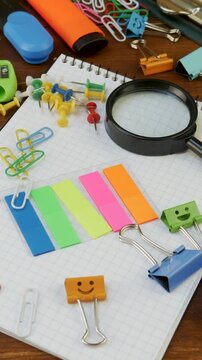 Magnifying glass, colored push pins, paper sticky notes on notebook with cells. Pencils, eraser, and push pins. Workspace setup with stationery essentials. Supplies for creativity, productive work