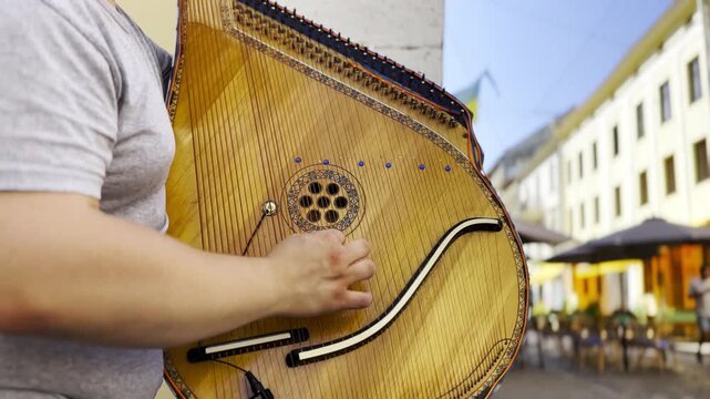 Male fingers of musician playing the bandura on a sunny summer day. Sunlight falls on the strings and wood surface, creating a warm and lively scene of outdoor music and authentic street performance