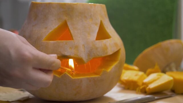 Small flame lights candle hidden within carved pumpkin. Jack-o-lantern shines with wicked grin. Halloween celebration begins with autumn harvest and flicker of light