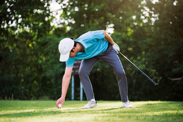 Asian golfer placing golf ball on tee before drive shot at golf course during morning round, preparation and precision in professional outdoor golf sport