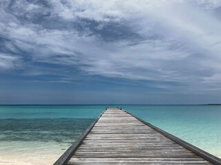 Fototapeta premium Wooden pier extending over tranquil turquoise water under blue sky 