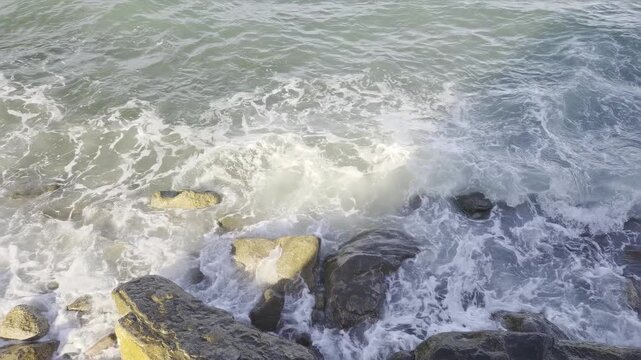 Aerial slow motion top down view of ocean waves crashing and receding over rocky shoreline in coastal intertidal zone