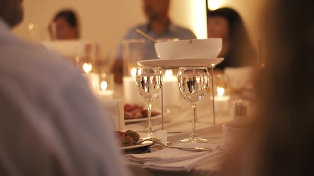 Glasses and table setting at candlelit wedding dinner with guests