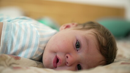 Baby lying on bed, looking towards camera with curiosity, relaxed and observant expression, early childhood exploration, warm and peaceful home setting