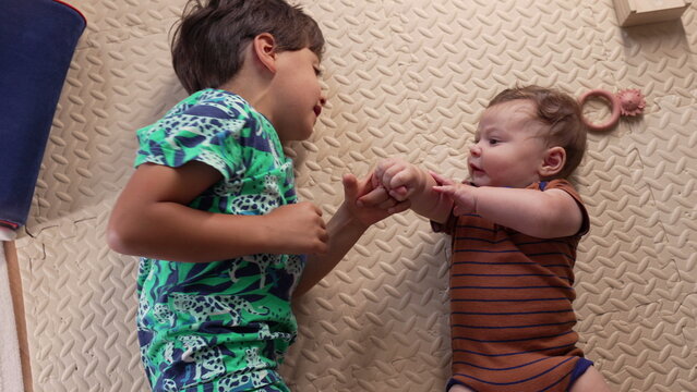 Young boy lying on mat, smiling at baby, playful sibling moment, affectionate interaction, warm childhood bonding, early family relationship, happiness and love