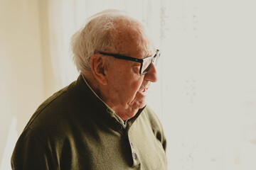 Fototapeta premium Elderly man with glasses looking through window at home