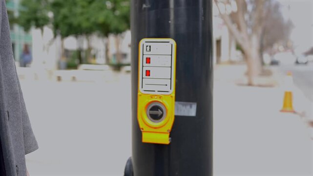 Female hand pressing pedestrian crossing button on urban street pole near crosswalk in city traffic area