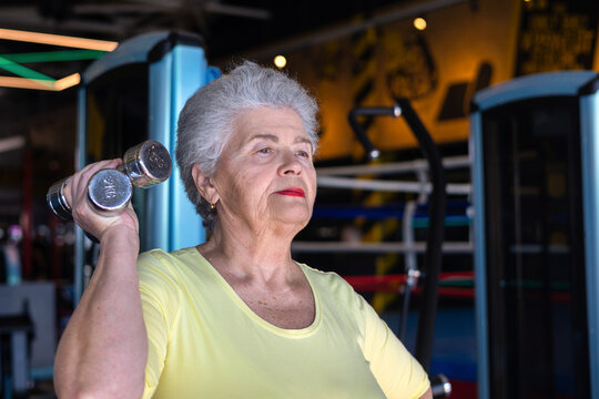 Active senior woman performing strength exercise with dumbbells in a gym. Concept of healthy aging, active lifestyle and fitness for older adults. Copyspace