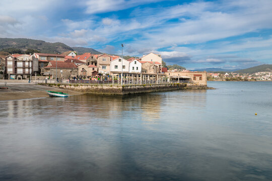 Combarro fishing village in Galicia, Spain with historic stone houses and iconic horreos on stilts reflecting in calm ria waters, mountains and blue sky beyond