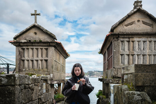 Young woman dipping a churro into a cup while exploring stone horreos in Combarro, finding joy during her travel experience in this traditional Galician village