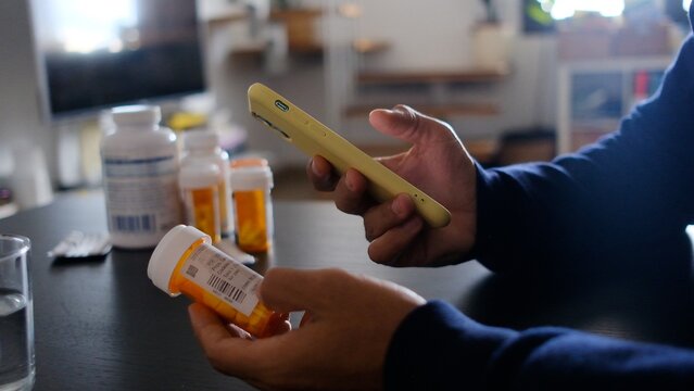 Person holding a prescription medicine bottle and scanning the barcode with a smartphone for medication management, tracking, and health monitoring through a digital application