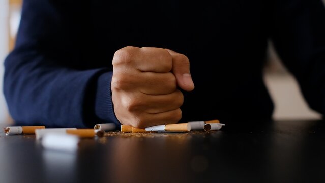 Person crushing cigarettes with a fist, symbolizing determination and willpower to stop smoking, breaking the habit for a healthier lifestyle, quitting addiction