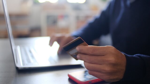 Person making a secure digital payment online, holding a credit card while typing on a laptop, providing financial information for an e-commerce transaction