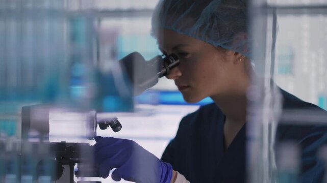 Female scientist in protective wear working in a medical research laboratory. Examining a sample under microscope
