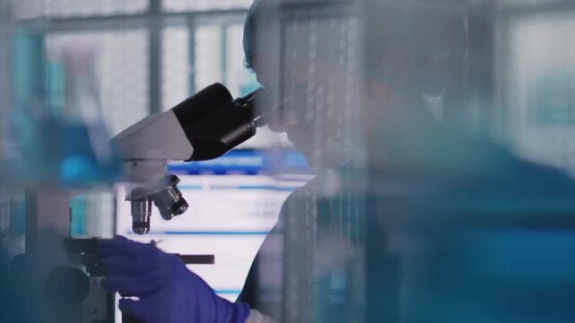 Female scientist in protective wear working in a medical laboratory. Examining a blood sample under microscope