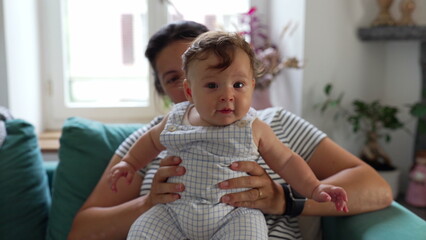 Baby sitting upright with mother’s support, early balance development, curious expression, interactive moment, parent-child bonding, trust, growth, care © Marco