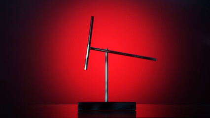Minimalist magnetic pendulum desk sculpture on a dark surface with dramatic red backlight. Modern...