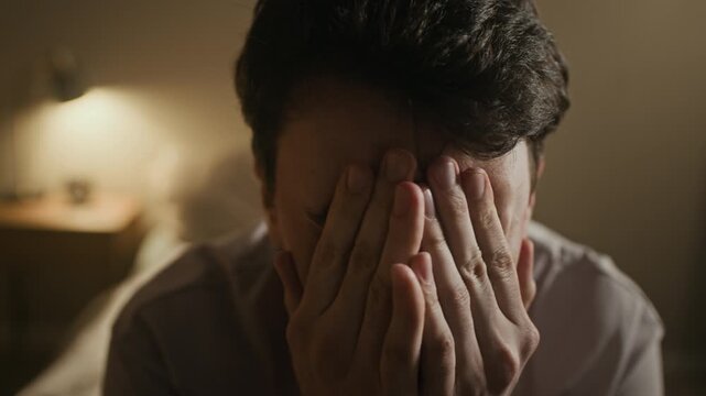 Close up shot of young overwhelmed Caucasian man loudly shouting while sitting in dimly lit bedroom at night