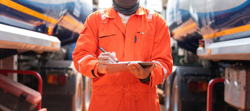 An engineer is checking on chemical hazardous material checklist to verify the safety condition with chemical road tanker as background. Industrial waorking scene, close-up and selective focus.