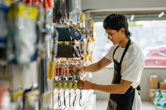 Young man wearing apron and glasses organizing products on a shelf in a hardware store