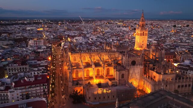 night drone orbiting shot of Seville cathedral with night illumination, Seville, Spain, famous Andalusian tourist landmark, Spanish Seville cathedral facade