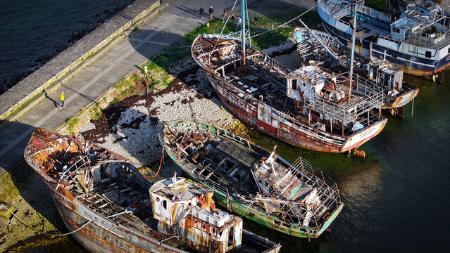 Aerial view of weathered, decaying boats resting on the shore, their rusted hulls a stark contrast to the calm, dark water, Le Sillon, Camaret-sur-Mer, Bretagne, France.