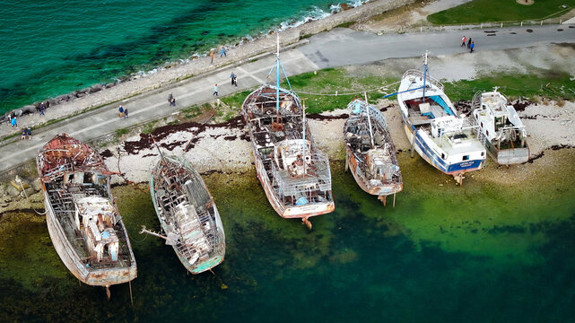 Aerial view of weathered boats resting on the shore where the tranquil turquoise sea meets the rugged coastline, Le Sillon, Camaret-sur-Mer, Bretagne, France.