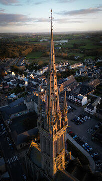 Aerial view of the spire of a gothic Kreisker chapel piercing the sky, casting long shadows over the town below, Saint-Pol-de-Leon, Bretagne, France.