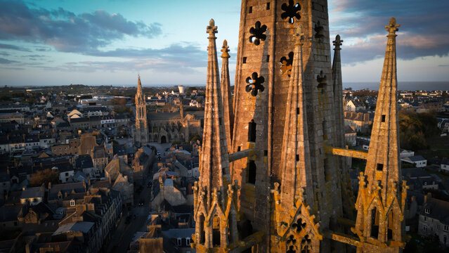 Aerial view of the imposing Kreisker chapel spire casting shadows over the quaint rooftops, a symphony of stone and sky, Saint-Pol-de-Leon, Bretagne, France.
