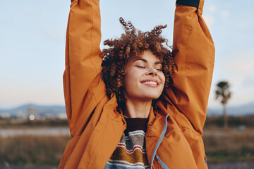 Happy woman with curly hair wearing rainbow sweater and orange jacket smiles with eyes closed...
