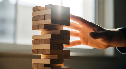 A person carefully balancing wooden blocks in a precarious tower structure near a sunny window