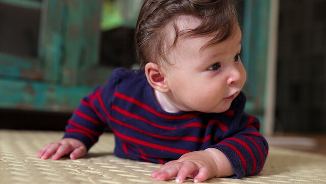 Baby lying on tummy, smiling with excitement, looking directly at camera, joyful expression, early crawling stage, curiosity, playfulness, home environment, infant development