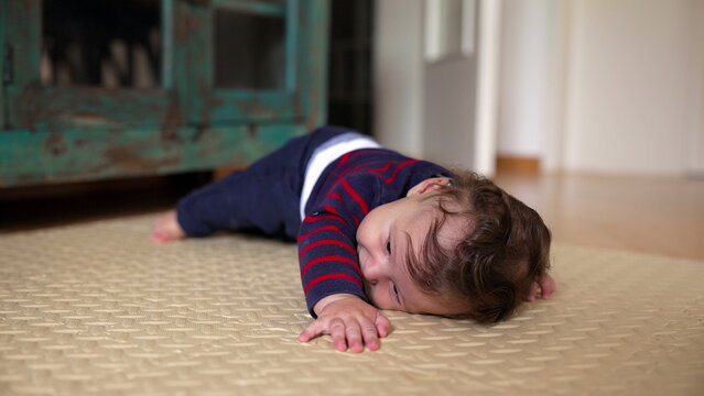 Baby lying on mat, attempting to crawl forward, determined expression, early movement stage, curiosity, exploration, playful learning, family home environment, development
