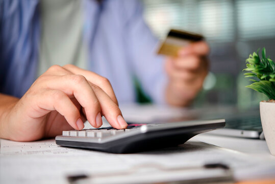 Close up of businessman hand using calculator and holding credit card for online payment at office desk. Concept of personal finance, accounting, budget planning, shopping and financial expense.