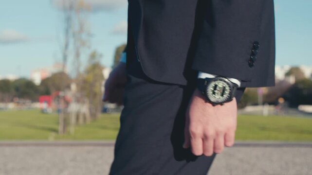 Close-up of a man's hand with a watch on his wrist, who is dressed in a dark blue business suit and walking along a city street. Real time video.