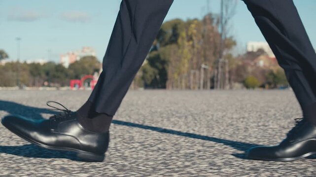 Side, close-up view to the businessman in a black new classic shoes walks on the street. Legs of a businessman in fashionable shoes walking, outdoors. Business concept. Stylish men wears. Low angle